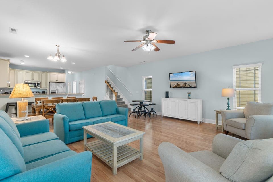 Relax in your spacious living room with vibrant turquoise seating and warm wood floors, perfectly positioned near the open kitchen.