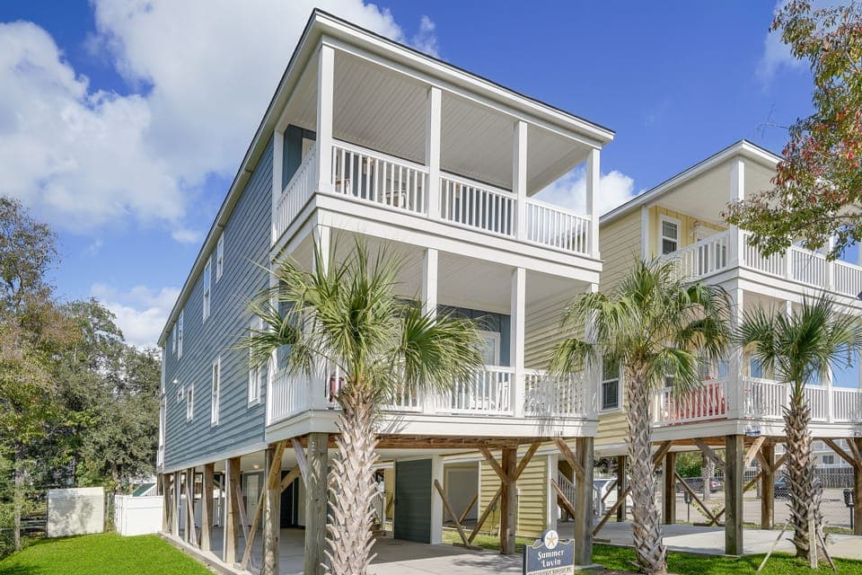 Modern beach house with elevated design, covered parking, and tropical palm landscaping creates an inviting coastal retreat.