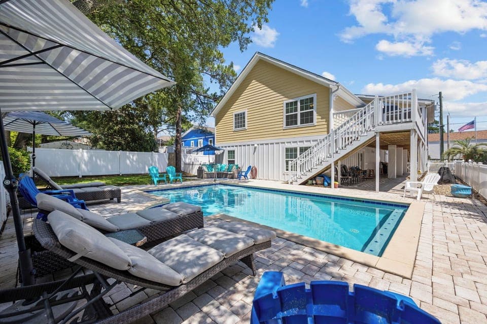 Private pool paradise awaits with comfortable loungers, shaded areas, and a charming two-story home backdrop for your perfect getaway.