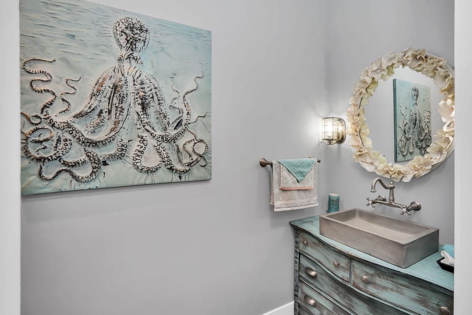 Freshen up in this beautifully designed powder room with coastal-inspired artwork and elegant shell-framed mirror.