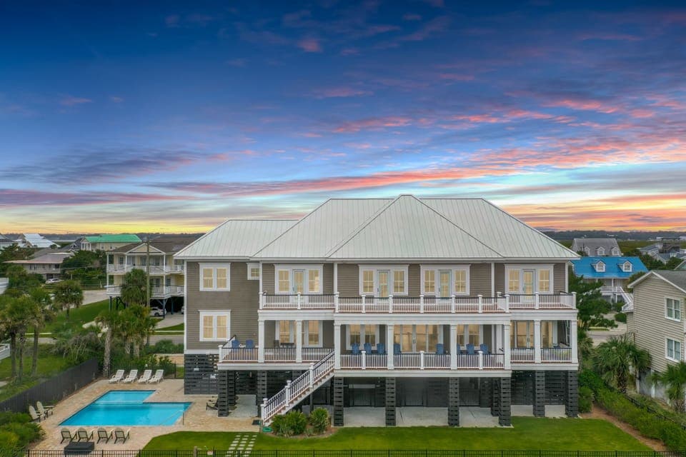 Stunning beachside property featuring multiple balconies, private pool, and coastal architecture under vibrant sunset skies.