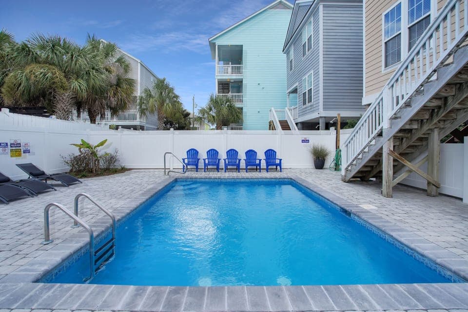Dive into your private oasis! This sparkling pool awaits with cheerful blue chairs and tropical palms surrounding your perfect getaway.