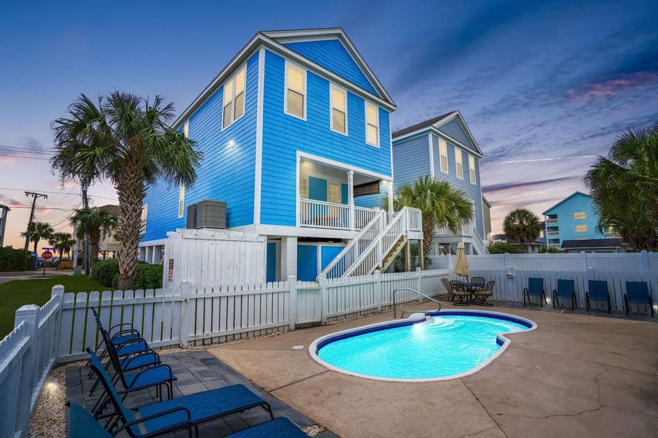 Bright blue coastal home with private pool and tropical palm trees in a beachside neighborhood.