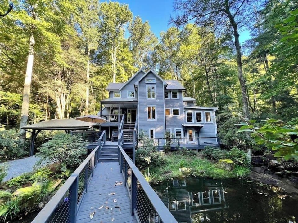 Modern house surrounded by trees with a wooden bridge over a pond