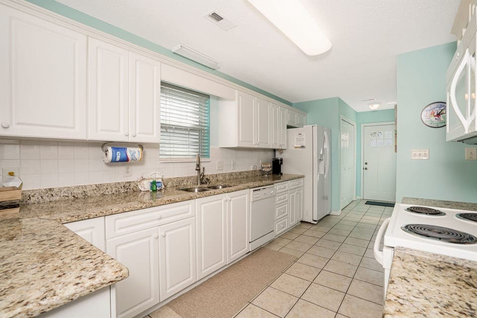 Your fully-equipped kitchen awaits with granite countertops, white cabinetry, and modern appliances for preparing memorable meals during your stay.