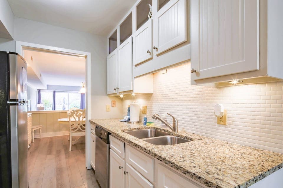 The galley-style kitchen features white cabinetry, granite counters and tiled backsplash.