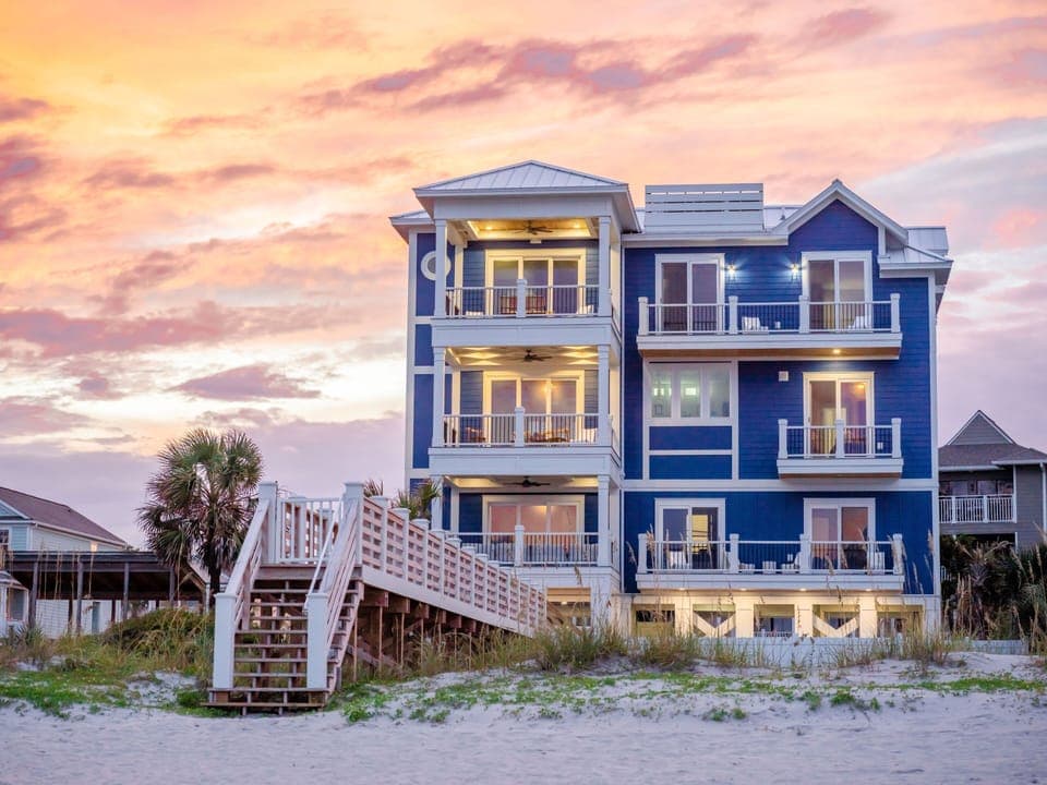 Stunning beachfront property with vibrant blue siding and multiple balconies overlooking pristine sandy shores during golden hour.