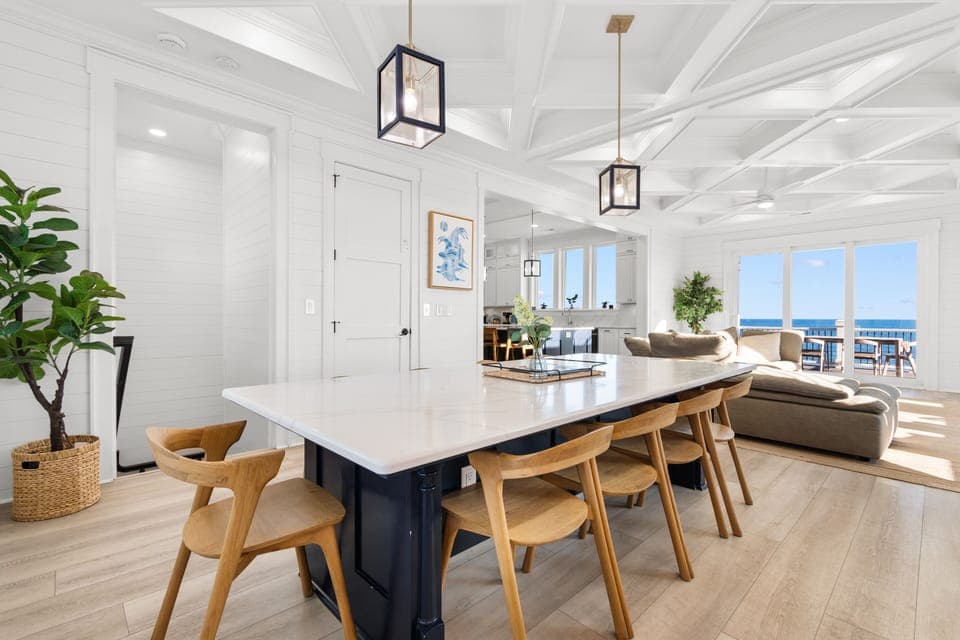 Your open-plan living space flows beautifully with coastal light streaming through floor-to-ceiling windows, creating the perfect spot for memorable meals and relaxation.