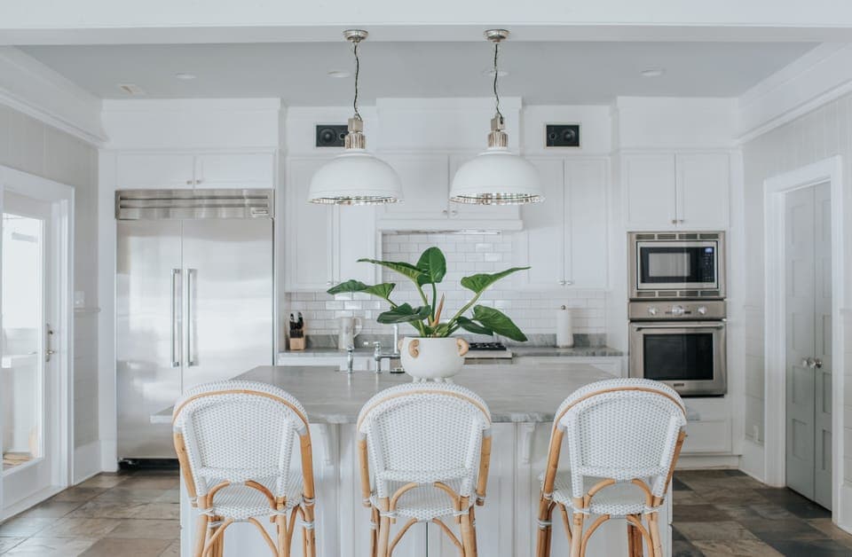 Kitchen island with three bar stools, thermador refrigerator, stove and oven on the far wall.