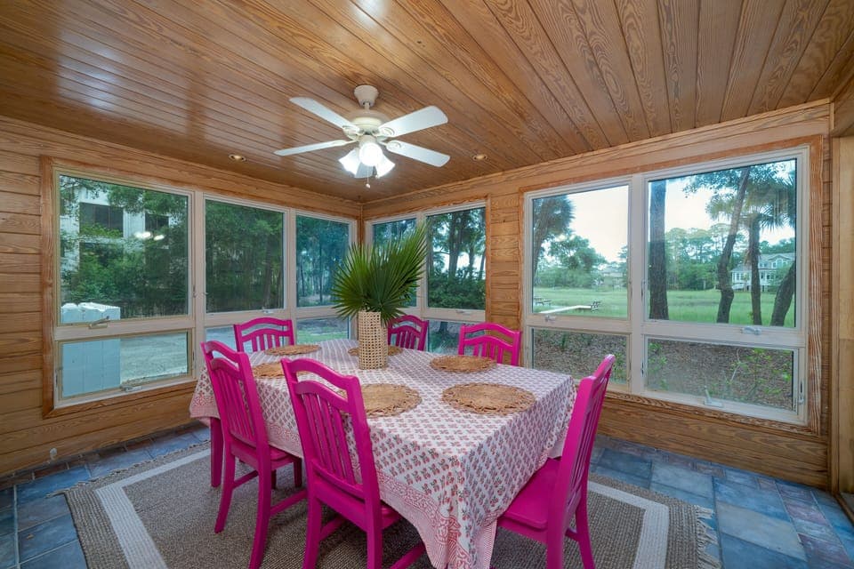 The room has floor to ceiling windows on three walls. A dining table can seat 8