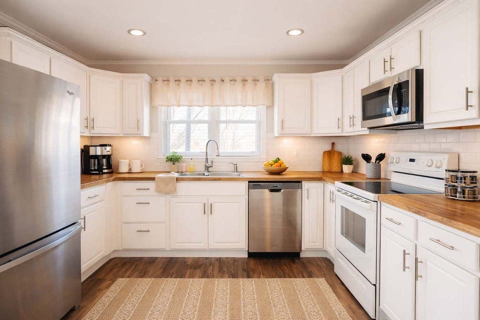 Bright, fully equipped kitchen with stainless steel appliances, warm wood countertops, and crisp white cabinetry. Enjoy a clean, inviting space perfect for cooking, coffee, and gathering.